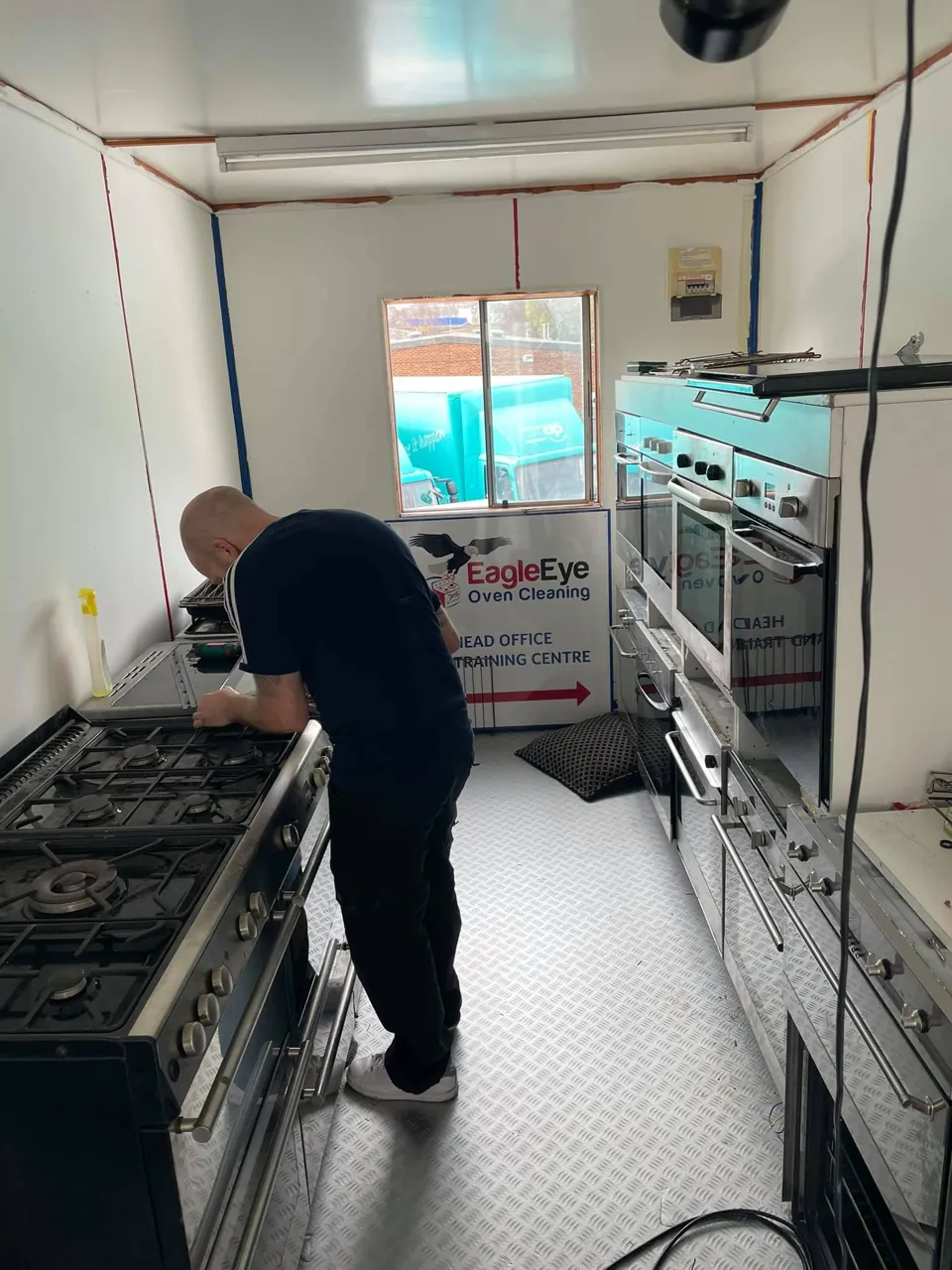 A trainee working at a row of cookers and built-in ovens in the training workshop